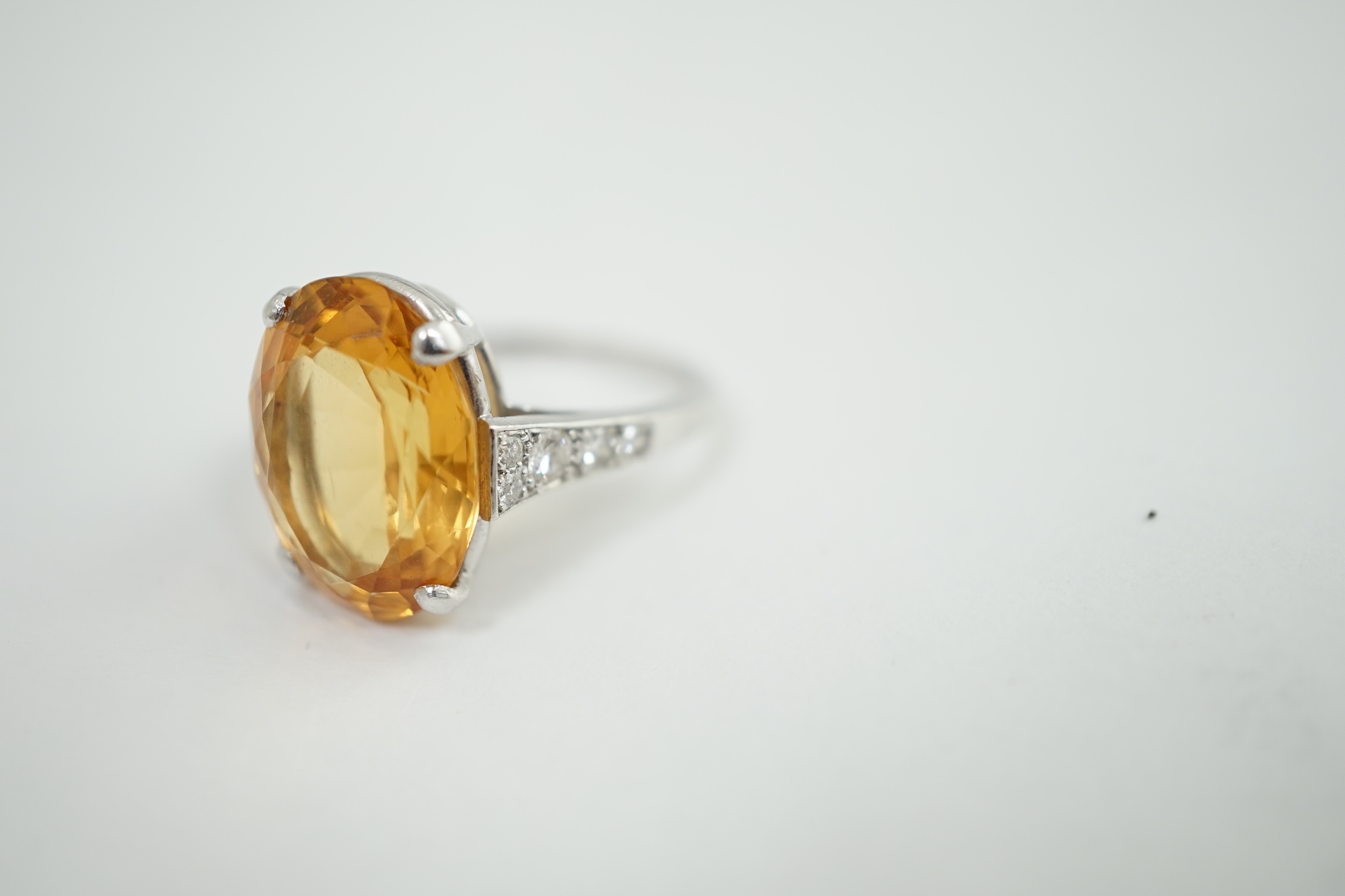 A 1940's platinum? and single stone oval cut imperial? topaz set dress ring, with ten stone graduated round cut diamond set shoulders